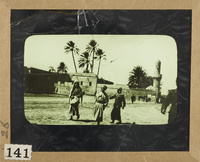 Three villagers standing outside the city walls of an Arab village; in the background a minaret and Palm trees